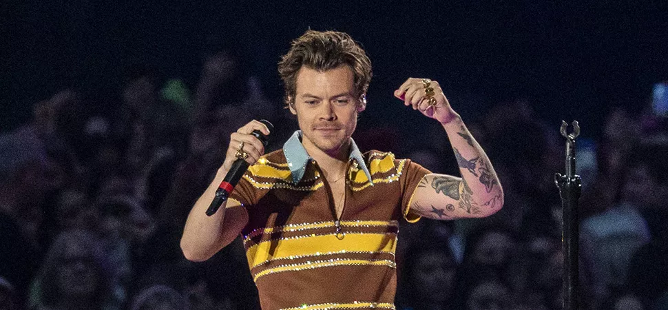 Harry Styles in einem gestreiften Oberteil und Mikro in der Hand auf der Bühne