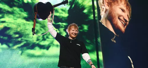 Ed Sheeran hält eine Gitarre in die Luft und freut sich.