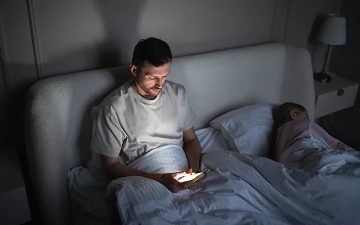 Ein Mann liegt im Bett und scrollt auf seinem Handy.